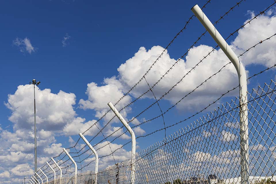 A metal fence with barbed wire lines against the background of a blue sky with clouds