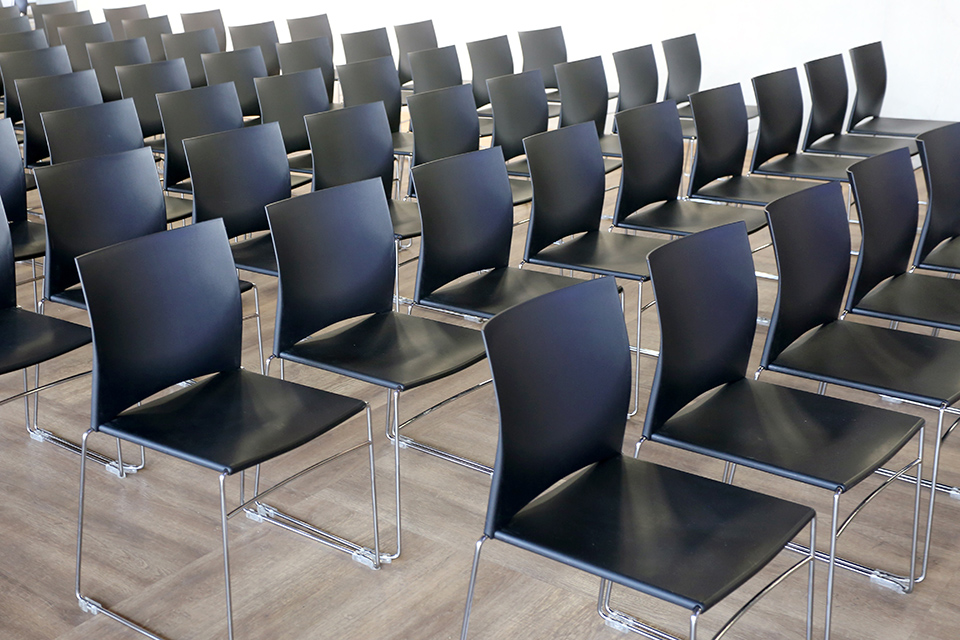 Schwarze Stühle stehen in Reihen auf einem Laminatboden.