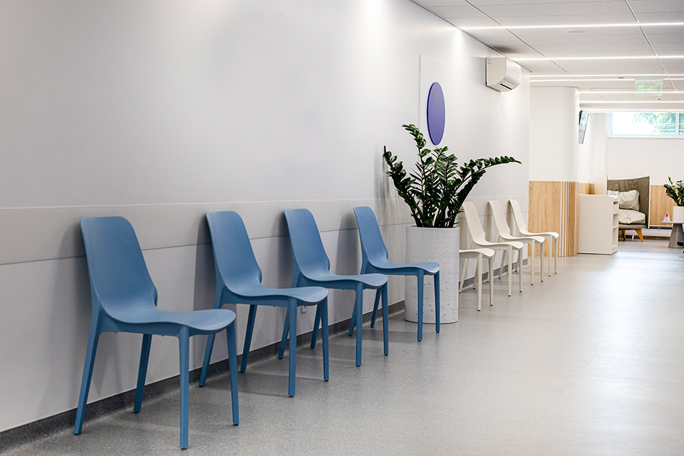 Blaue Stühle in einem Flur zur Wand stehend. Der Boden ist aus Linoleum.