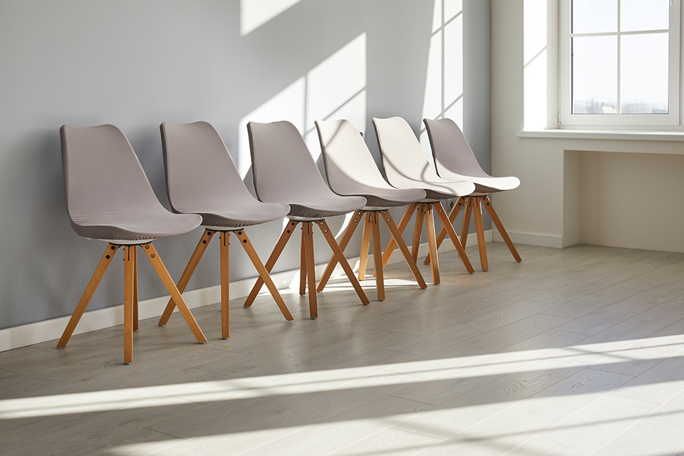 Abgebildet sind sechs bequeme graue Plastikstühle mit Holzbeinen in einem schlichten, minimalistischen Interieur ohne Personen auf hellgrauem Vinylboden.