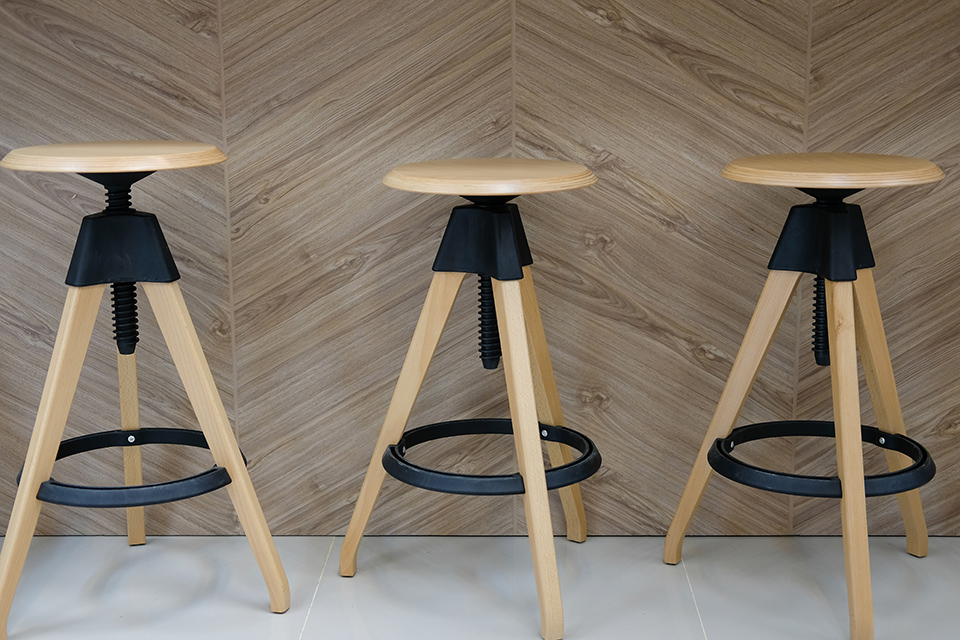 Es stehen drei Holzhocker auf hellgrauen harten Keramikfliesen.