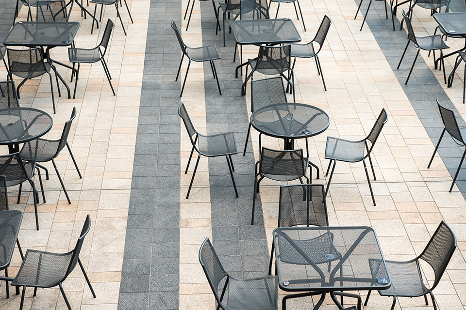 Im Außenbereich sind Stühle und Tische nebeneinander auf harten, glatten Natursteinen aufgestellt.