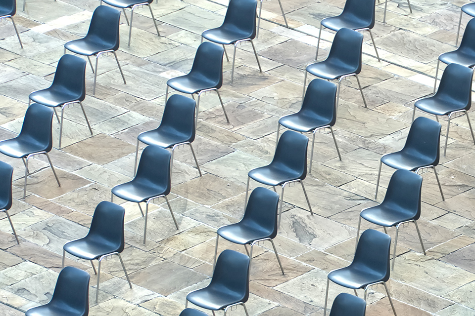 Im Freien stehen weit auseinanderstehende Stuhlreihen auf graubraunen, harten und rauen Natursteinen.