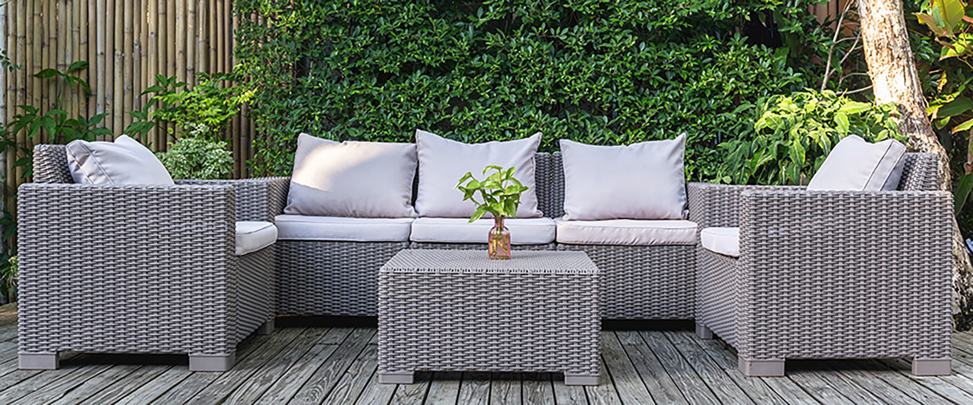 Große Terrasse mit Rattan-Gartenmöbeln im Garten auf Holzboden und einem grünen Busch im Hintergrund