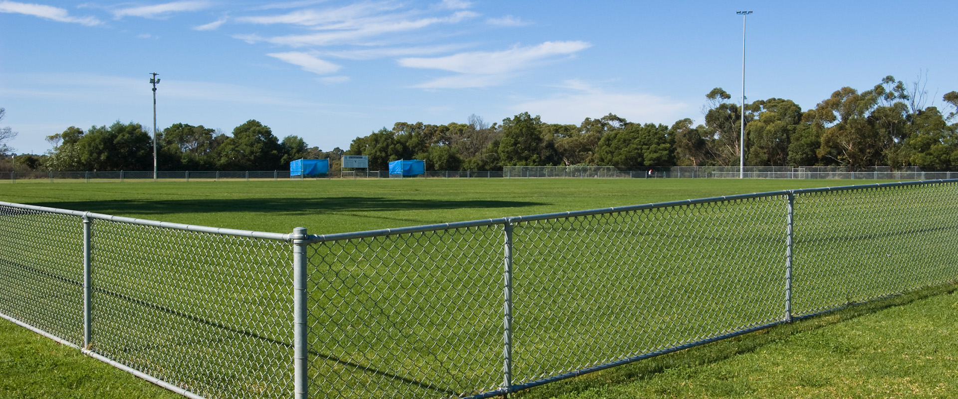 Large sports ground, football pitch with a grassy area, enclosed by a grey wire mesh fence